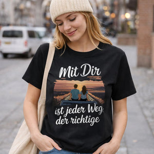 Junge Frau trägt schwarzes Bio-Shirt mit Roadtrip-Illustration eines Paares und dem Spruch „Mit Dir ist jeder Weg der richtige“ – nachhaltiges Bright Light Arts Damen-Shirt für Liebe, Reisen und Alltag.