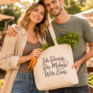 Natürlicher Jutebeutel mit dem Liebes-Statement „Ich Deins. Du Meins. Wir Eins.“ getragen von einem glücklichen Paar auf einem Wochenmarkt – minimalistisches Geschenk für Paare