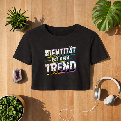 Schwarzes Cropped T-Shirt mit Aufdruck „Identität ist kein Trend“ im Bright Lights Arts Mockup auf Holzuntergrund mit Pflanzen, Kristall und Kopfhörern