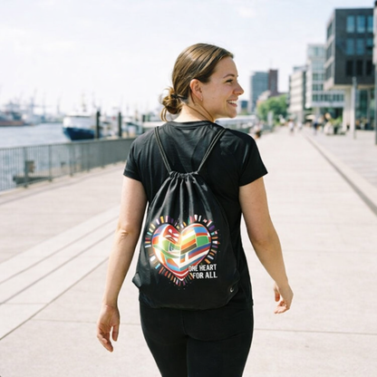 Frau trägt den schwarzen Inner Fire Gym Bag auf dem Rücken in einer sonnigen Umgebung; das Sonnenlicht lässt das Flaggen-Mosaik leuchten