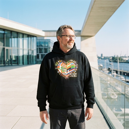 Person im schweren schwarzen Oversized Hoodie mit buntem Flaggen-Herz; helles Sonnenlicht lässt das Design energetisch pulsieren