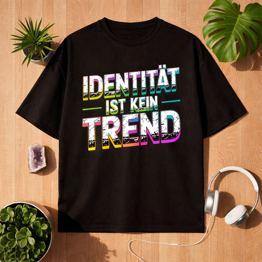 Schwarzes Oversized T-Shirt mit Statement Design „Identität ist kein Trend“ im Bright Lights Arts Lifestyle Mockup auf Holzuntergrund mit Pflanzen und Kopfhörern