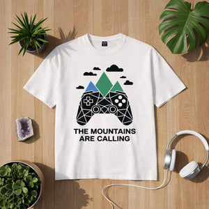„Bright Light Arts Premium T-Shirt The Mountains Are Calling – Gaming Edition mit Controller- und Bergmotiv, Lifestyle-Mockup auf Holzuntergrund“