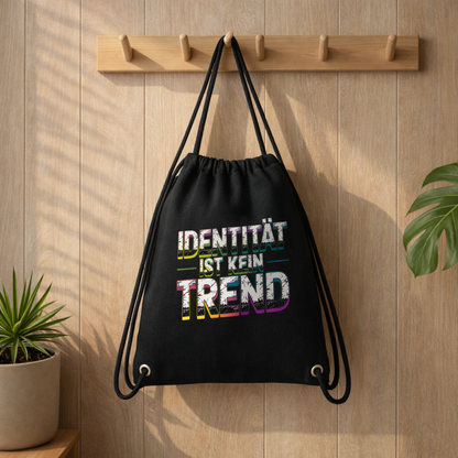 Schwarzer Gym Bag mit „Identität ist kein Trend“ Design von Bright Lights Arts, aufgehängt an Holzleiste in warmem Lifestyle Mockup mit Pflanzen und natürlichem Licht