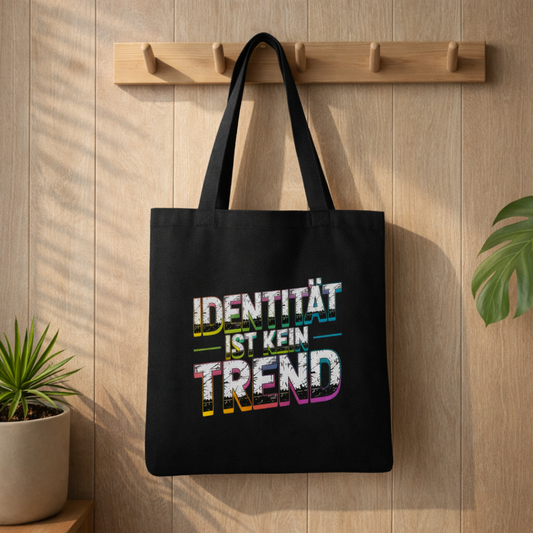 Schwarzer Jutebeutel mit „Identität ist kein Trend“ Design von Bright Lights Arts, aufgehängt an Holzleiste in warmem Lifestyle Mockup mit Pflanzen und natürlichem Licht