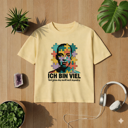 Hellgelbes Kinder T-Shirt mit „Ich bin viel“ Autismus Puzzle Portrait Design als Flatlay auf hellem Holzboden mit Pflanzen und Kopfhörern – freundliches Lifestyle Mockup