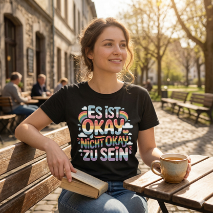 Person im schwarzen Bio-Baumwoll-Shirt mit dem Pastell-Schriftzug Es ist okay nicht okay zu sein.