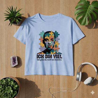 Hellblaues Premium Organic Damen T-Shirt im leicht taillierten Schnitt mit „Ich bin viel“ Autismus Puzzle Portrait Design als Flatlay auf hellem Holzboden mit Pflanzen und Kopfhörern – modernes Lifestyle Mockup