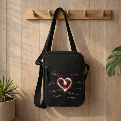 Schwarze Umhängetasche mit leuchtendem Herz Design und „I love you“ in verschiedenen Sprachen im Bright Lights Arts Lifestyle Mockup an Holz-Garderobe