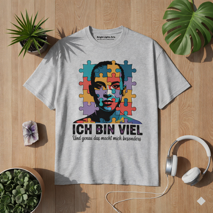 Graues T Shirt mit Ich bin viel Autismus Awareness Puzzle Design im natürlichen Lifestyle Mockup mit Holz Hintergrund, Pflanzen und Kopfhörern – Bright Lights Arts