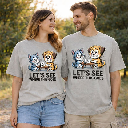 Verliebtes Paar trägt graue Oversized T-Shirts mit süßem Hund-und-Katze-Motiv beim ersten Date an einem Tisch mit Schild „1st Date“ und Schriftzug „Let’s see where this goes“, humorvolles Love-Design von Bright Light Arts.
