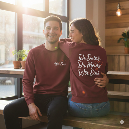 Paar in weißen Sweatshirts, einer zeigt den Brustdruck, einer den Rückendruck mit Wir Eins Statement, helles Licht