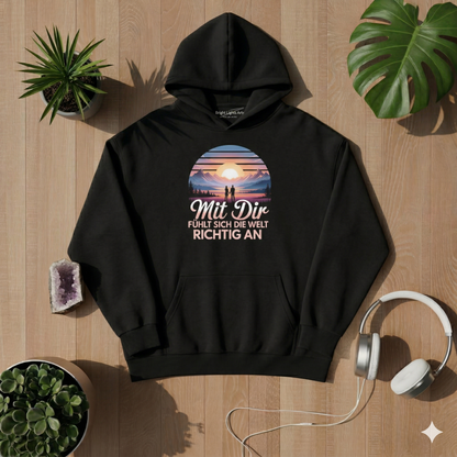 Draufsicht auf ein schwarzes oversized T-Shirt mit dem "Mit Dir fühlt sich die Welt richtig an" Design, umgeben von einem Amethyst-Kristall, weißen Kopfhörern, zwei Sukkulenten-Pflanzen und Monstera-Blättern auf einem hellen Holzhintergrund bei sonniger Lichtstimmung.
