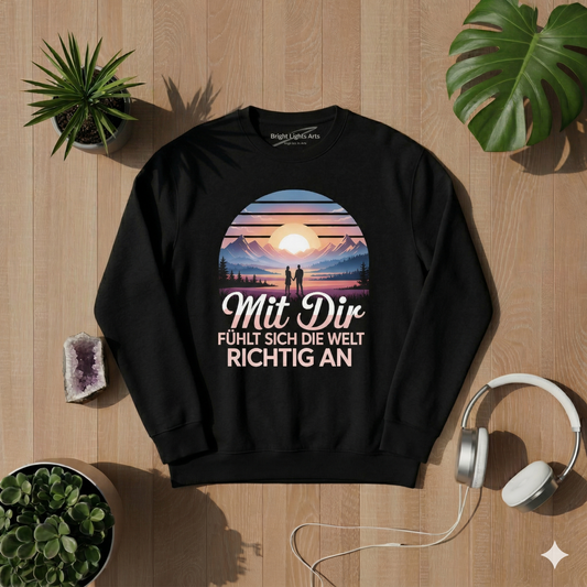 Draufsicht auf ein schwarzes premium Sweatshirt mit dem "Mit Dir fühlt sich die Welt richtig an" Design, umgeben von einem Amethyst-Kristall, weißen Kopfhörern, zwei Sukkulenten-Pflanzen und Monstera-Blättern auf einem hellen Holzhintergrund bei sonniger Lichtstimmung